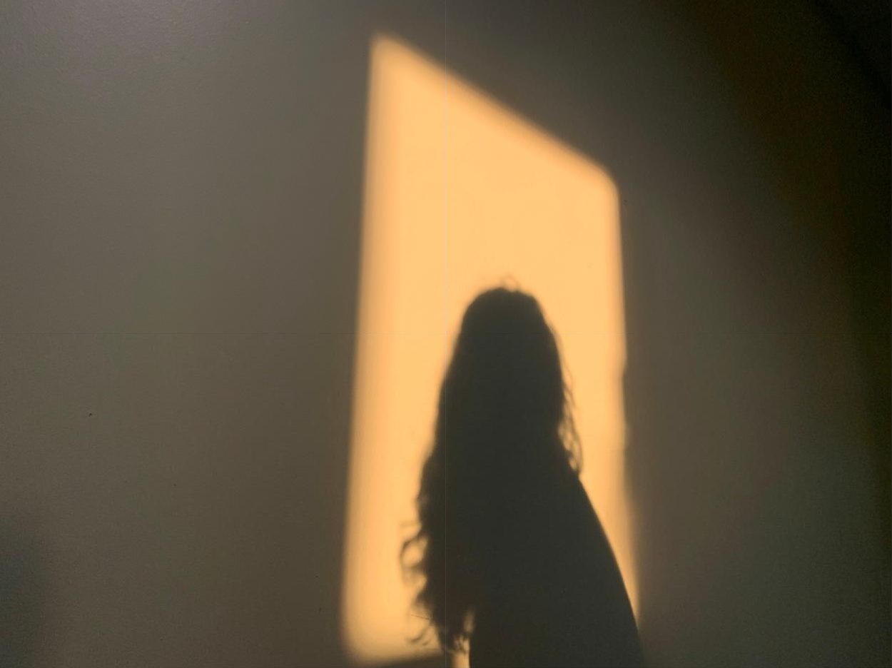 A woman's shadow inside a rectangle of warm evening light on a wall